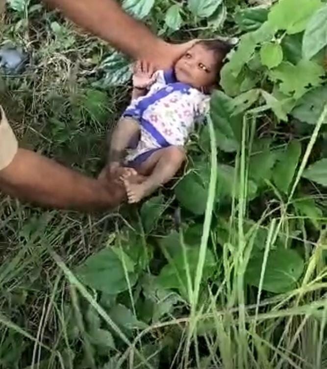 झाड़ियों में पड़ी बच्ची को उठाते हुए पुलिसकर्मी। स्रोत: ग्रामीण