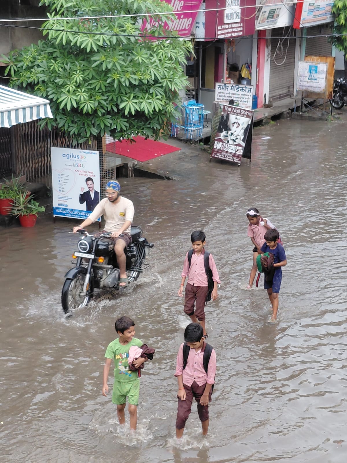 शहर के अशोक कॉलोनी में जलभराव के बीच जाते स्कूली बच्चे। संवाद