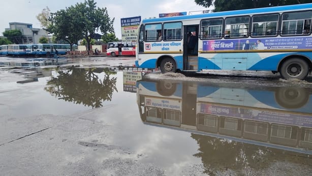 शहर के बस स्टैंड पर भरे पानी से गुजरती बस। संवाद