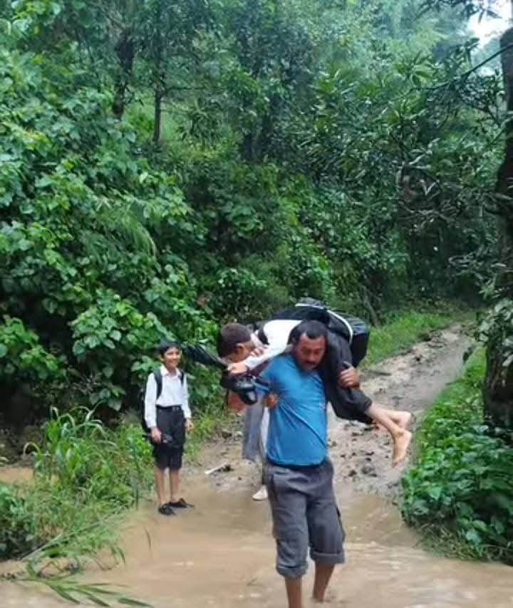 ग्राम पंचायत कचौली के बड्डू में स्कूली बच्चे को कंधे पर नाला पार कराता ग्रामीण। स्रोत: जागरूक प