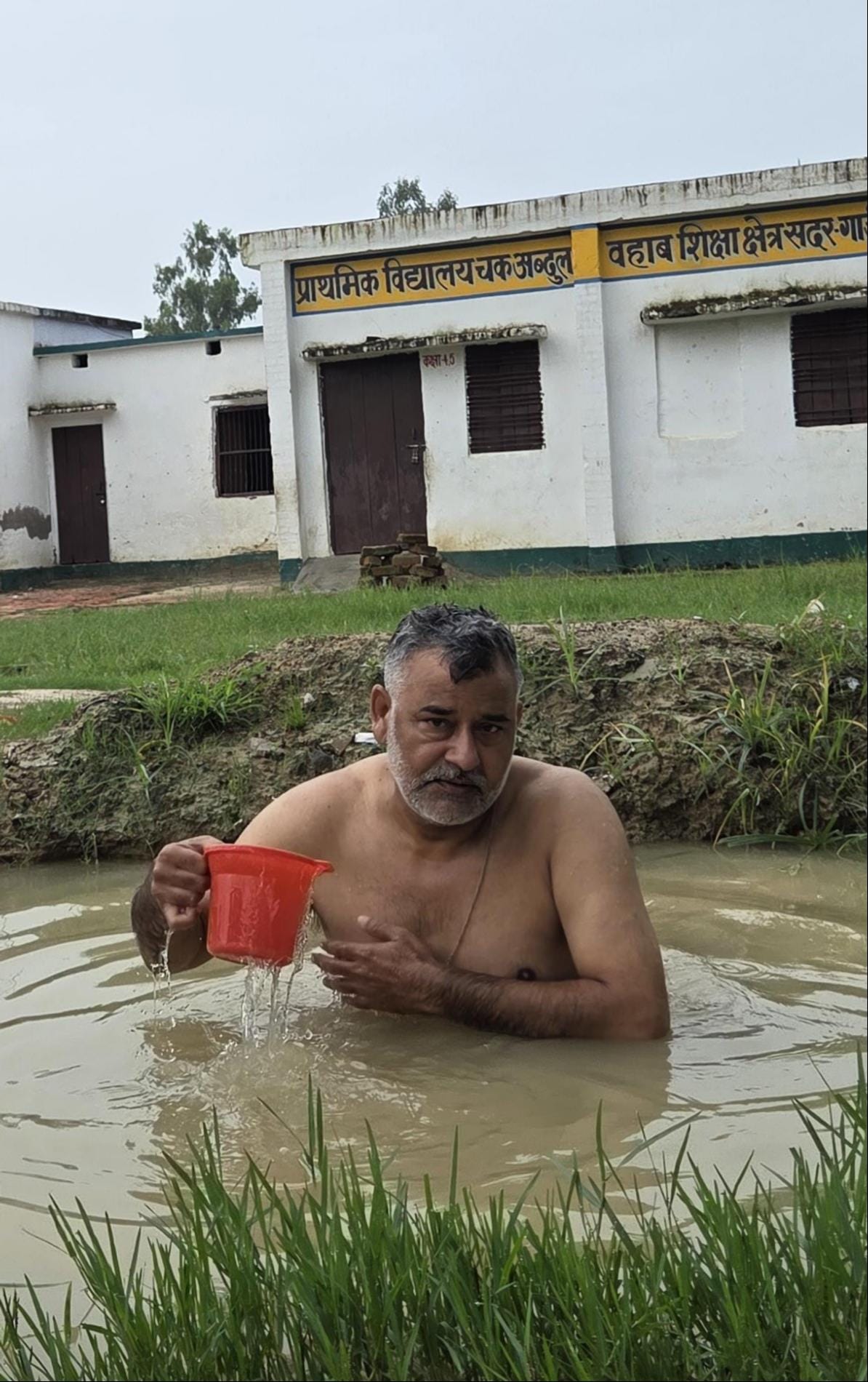प्राथमिक विद्यालय चक अब्दुल बहाव के परिसर में बने गड्ढे में नहाकर विरोध जाहिर करते समाजसेवी ब्र