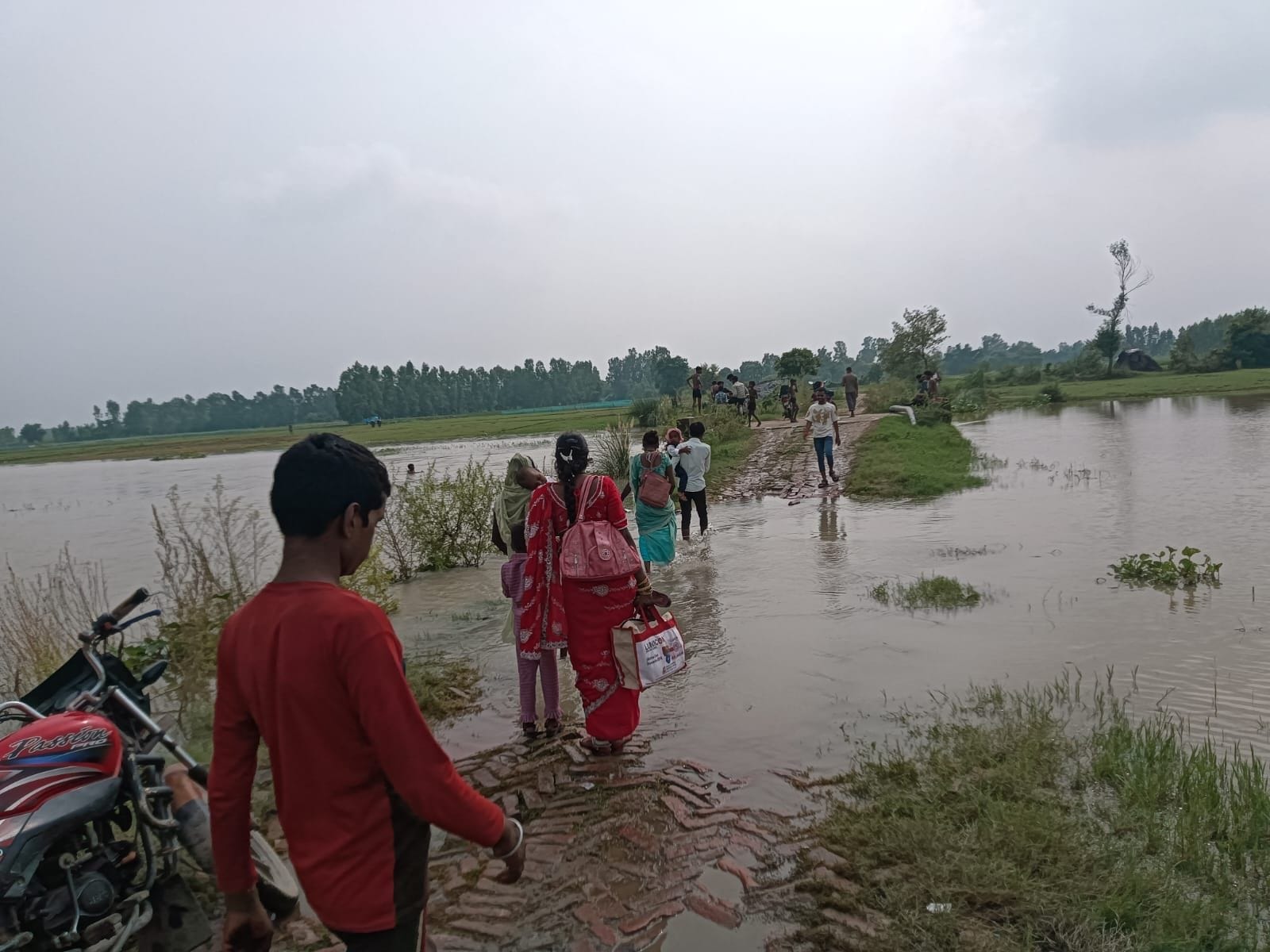 फोटो-24-फतेहपुर चौरासी में कबूलपुर मार्ग में भरे पानी से निकलतीं महिलाएं व ग्रामीण। संवाद