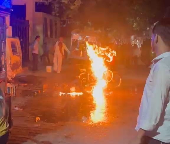बाइक में लगी आग को पानी डालकर बुझाते ग्रामीण