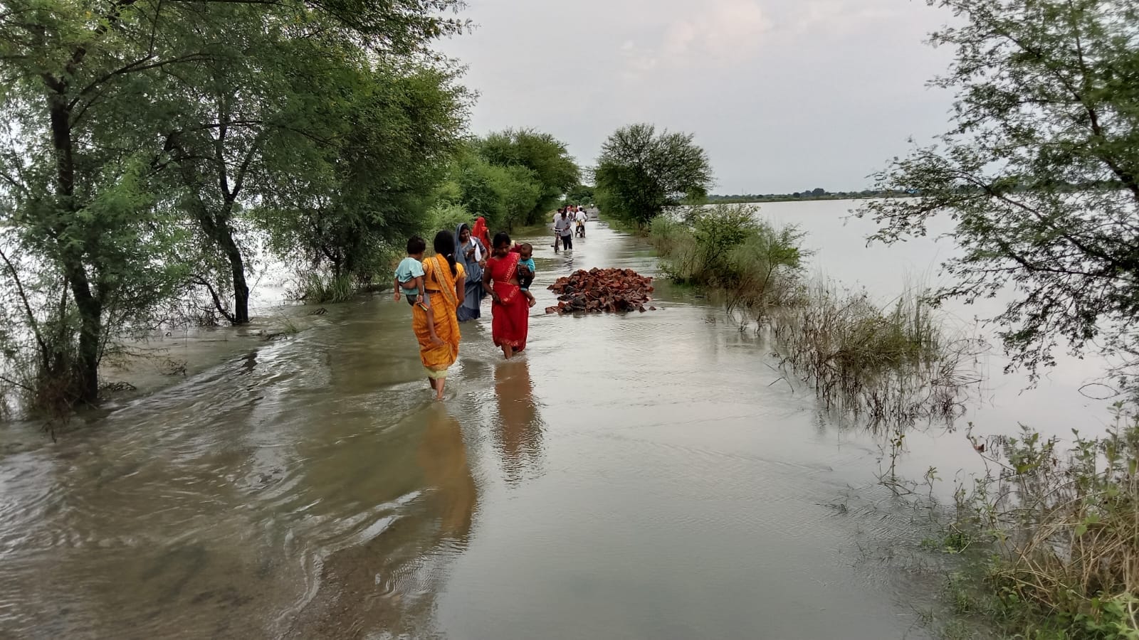 रेवतीपुर-मां कामाख्या धाम पर चढ़े बाढ़ के पानी से बच्चों को गोद में लेकर निकलती महिलाएं। संवाद