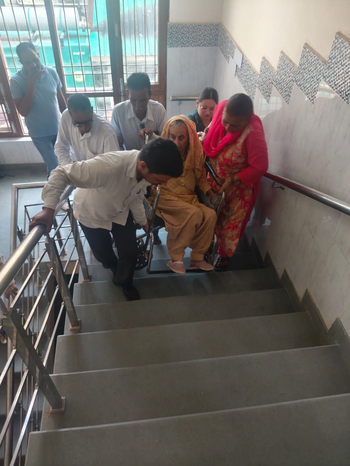 घुमारवीं अस्पताल में रैंप और लिफ्ट न होने से मरीज को व्हीलचेयर के साथ उठाकर ले जाते परिजन। संवा
