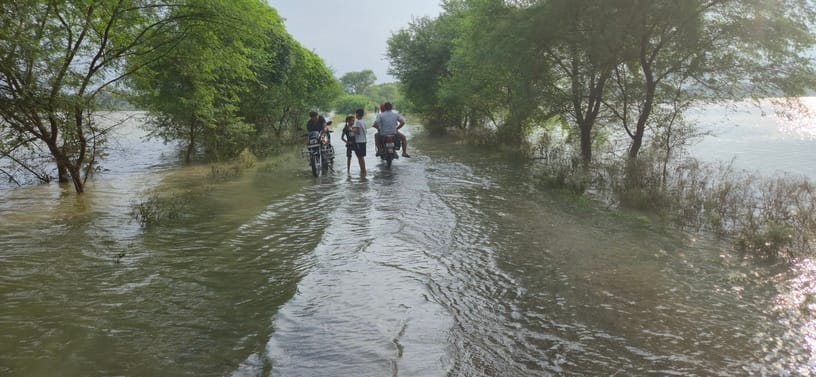 रेवतीपुर-रामपुर मार्ग पर फैले बाढ़ के पानी से गुजरते राहगीर। संवाद