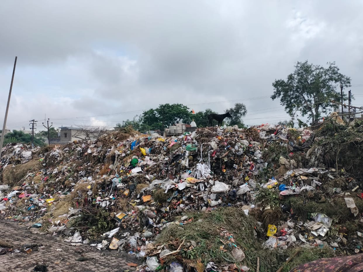 Garbage pile taking the shape of a mountain; people in distress due to the stench.