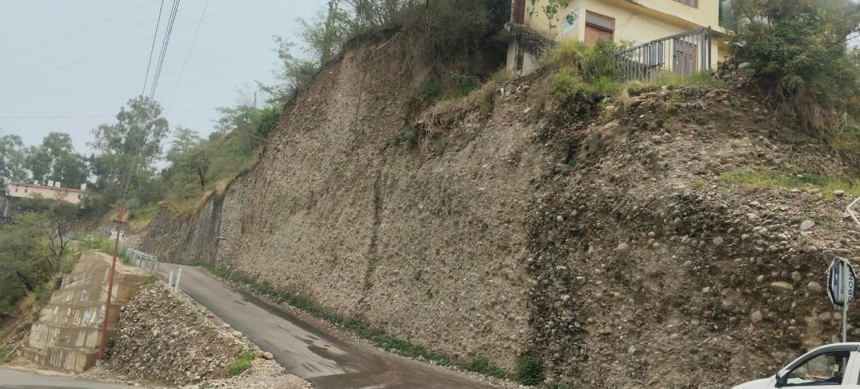 Retaining wall and railing work incomplete at Oohal Chowk; journey fraught with risk due to potholes.