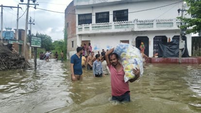 फोटो-19- बीघापुर के पोरई गांव में लोन नदी में आई बाढ़ के बाद घर से सामान लेकर जाता युवक। संवाद