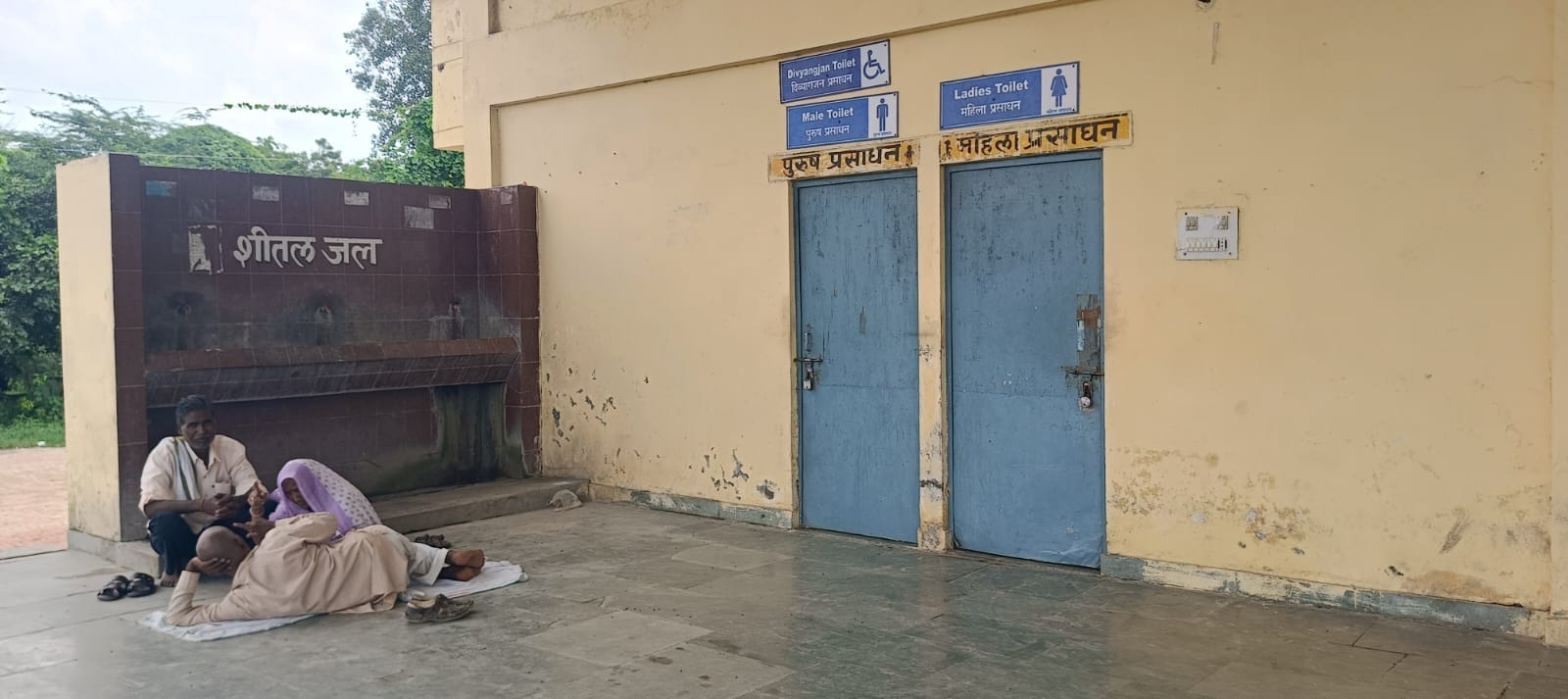 स्टेशन के शौचालय में लटका ताला और उसके सामने जमीन पर बैठे यात्री।संवाद