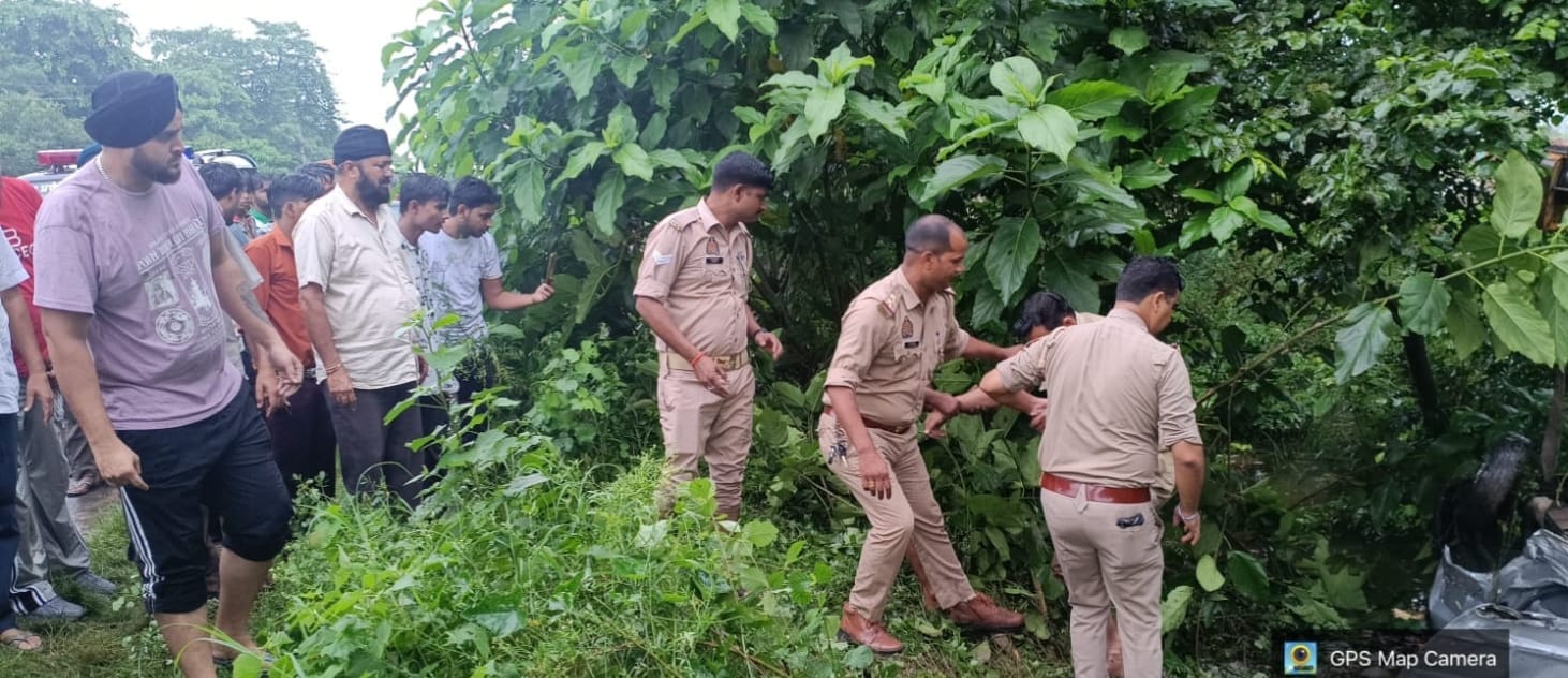 असम हाईवे किनारे पानी से भरे गड्ढे में घुसी कार को देखते पुलिसकर्मी और अन्य -संवाद