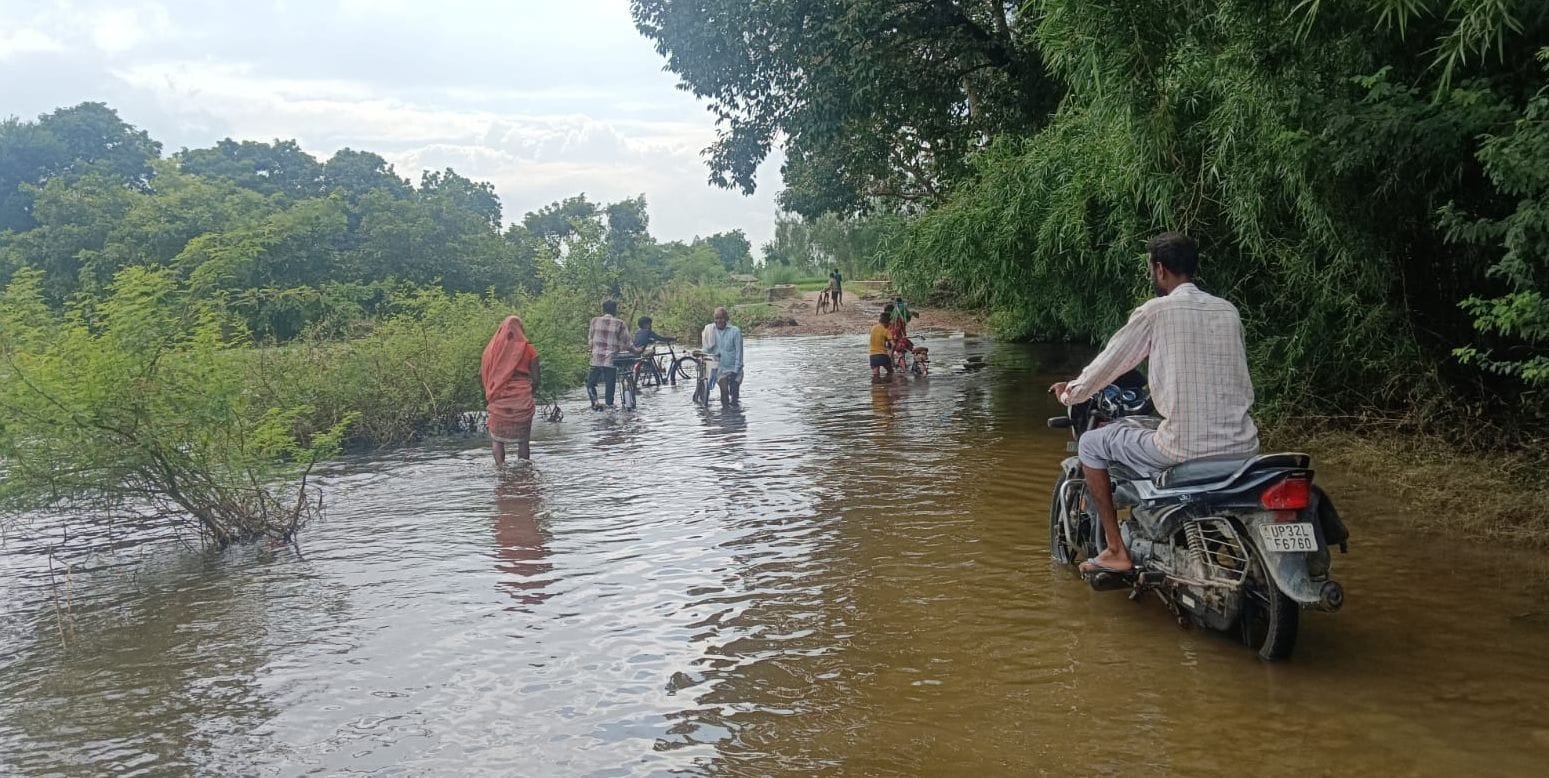 हलोर के गऊघाट से मझिगंवा जाने वाली मुख्य सड़क पर भरे पानी से होकर निकलते लोग। 