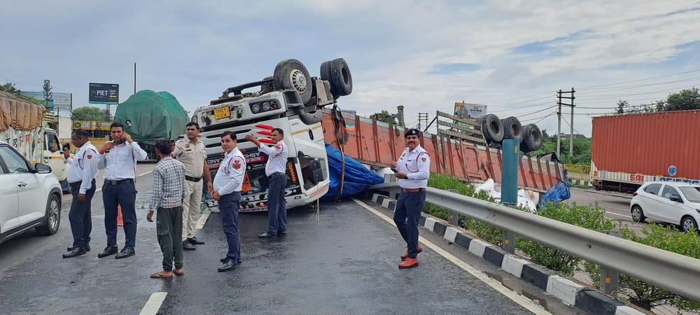 Trailer overturns after hitting divider near Pattikalyana village; traffic jam ensues.