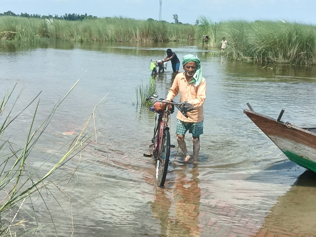 सोनौरा संपर्क मार्ग पर पानी से साइकिल लेकर गुजरते लोग।