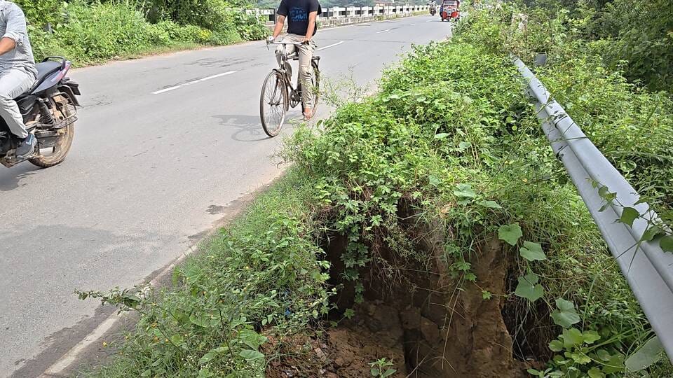Road caves in due to rain; ten foot-deep pit poses accident risk.