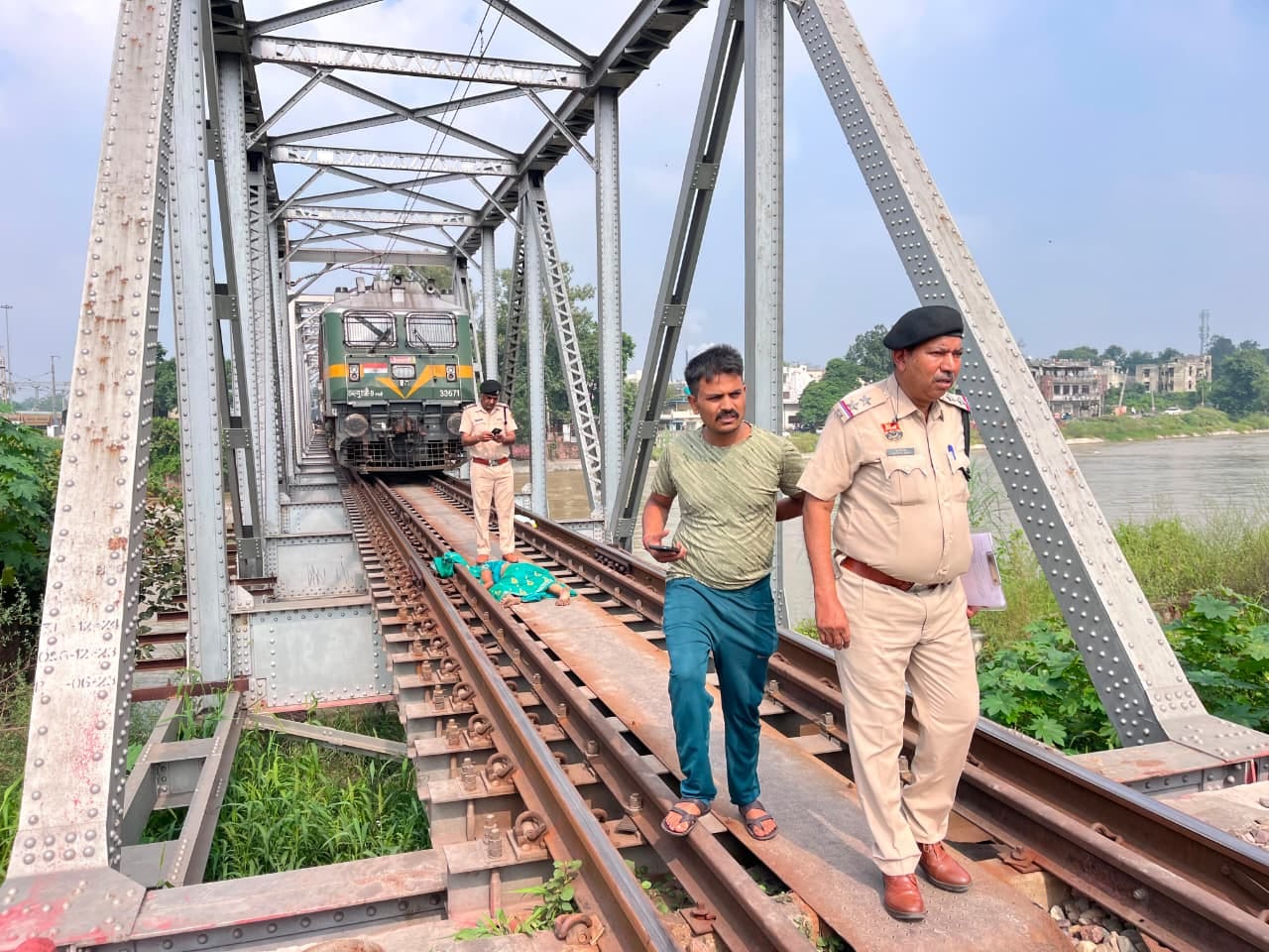 पुल के रेल ट्रैक पर पड़ा महिला का शव, रोकी गई ट्रेन और जांच करती पुलिस। संवाद