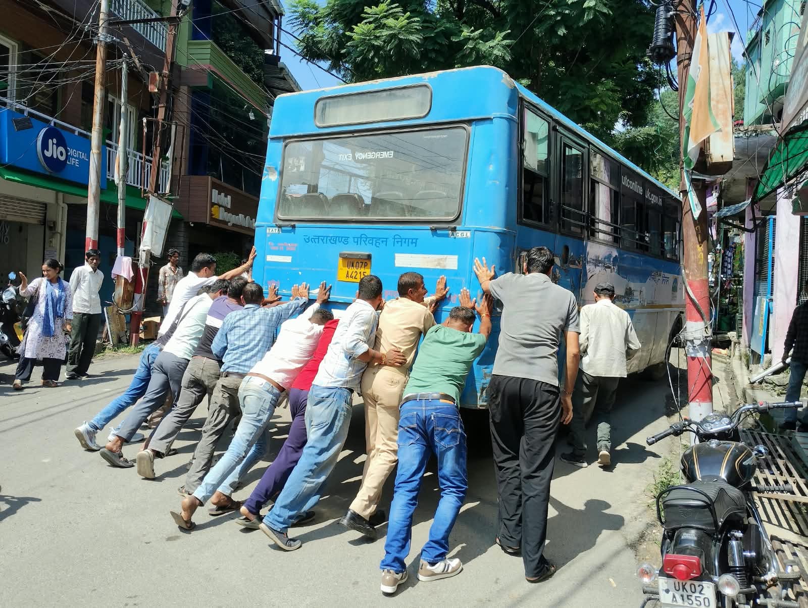 बागेश्वर में कोतवाली के पास खराब बस को धक्का लगाकर किनारे करते लोग। संवाद