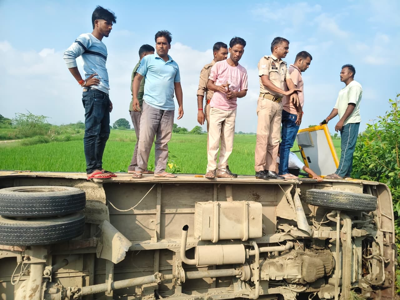 सड़क किनारे पलटी पड़ी बस के ऊपर खड़े लोग। संवाद