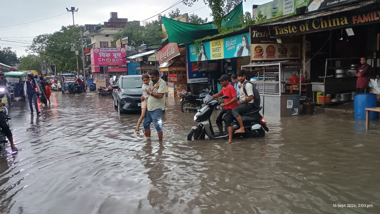 शहर के लंका तिराहा के पास बच्चे को गोद में लेकर जलभराव के बीच से निकलता युवक। संवाद