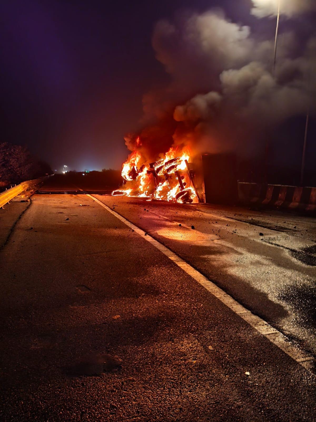 Truck loaded with gravel overturns after hitting divider; catches fire.