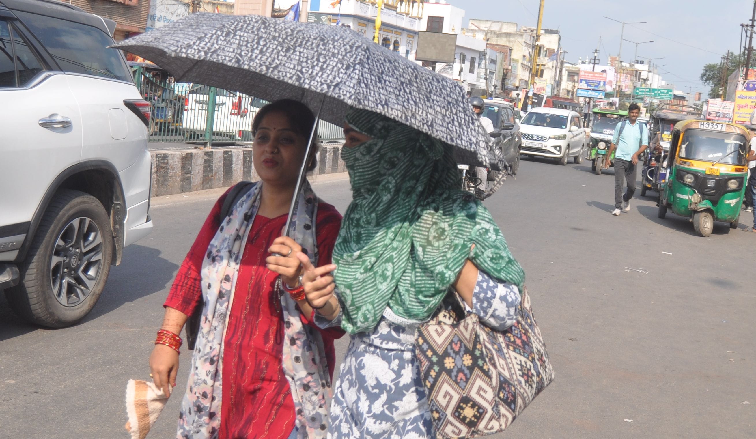 दिल्ली रोड पर धूंप से बचने के लिए छाता लगाकर सड़क पर जाती युवतियां। संवाद