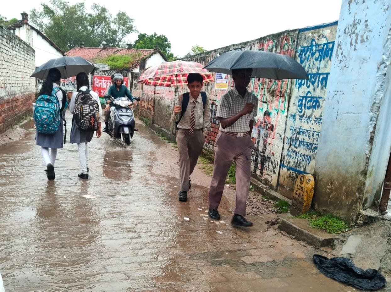 सुबह बारिश के दौरान छाता लेकर स्कूल जाते छात्र-छात्राएं। संवाद