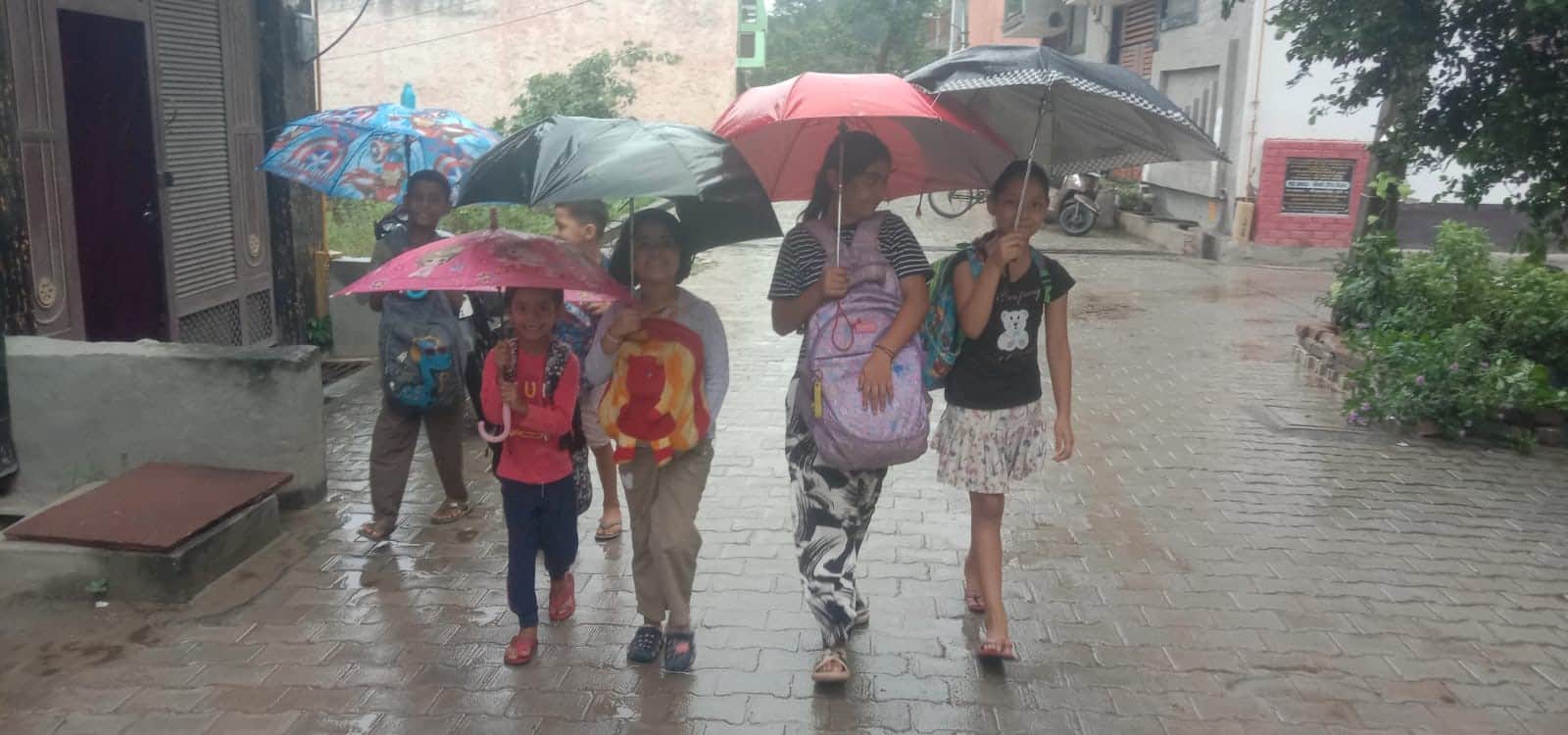 बारिश से बचने के लिए छाता लगाकर ट्यूशन जाते बच्चे