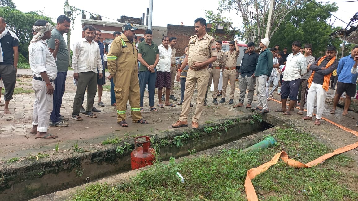 फोटो - 01 आग बुझने के बाद पड़ा सिलिंडर व मौजूद दमकल टीम। संवाद