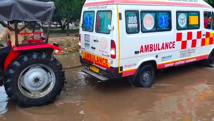 Ambulance stuck in water-filled pothole on highway; pulled out using a tractor.