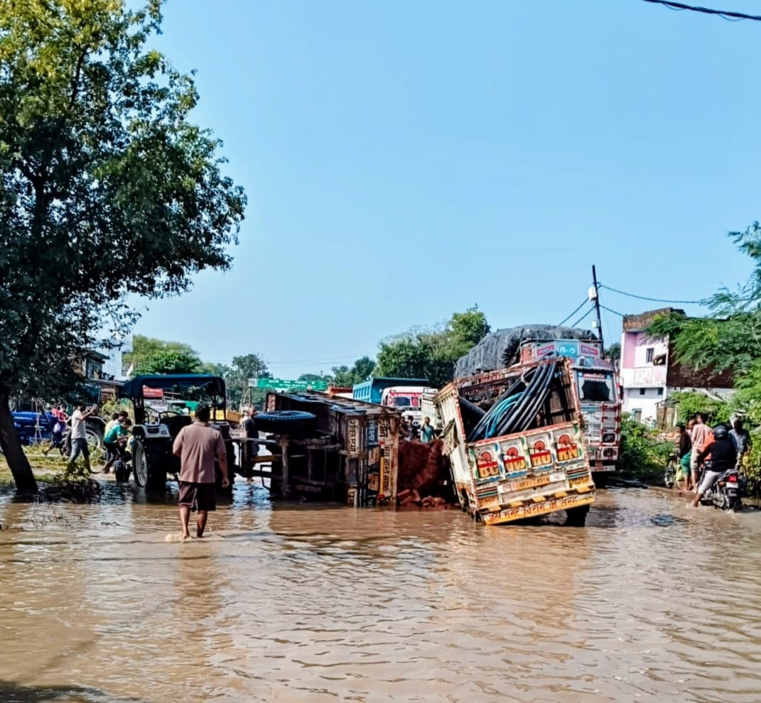 Highway riddled with potholes and waterlogging; brick-laden trolley overturns, loaders get stuck.