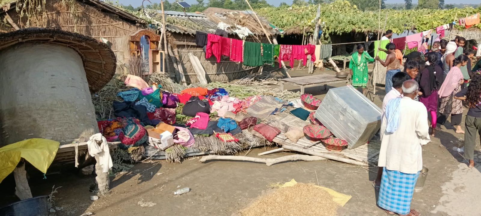 बाढ़ के पानी से खराब हुए बेड और कपड़ों को घर के सामने सुखाते लोग।