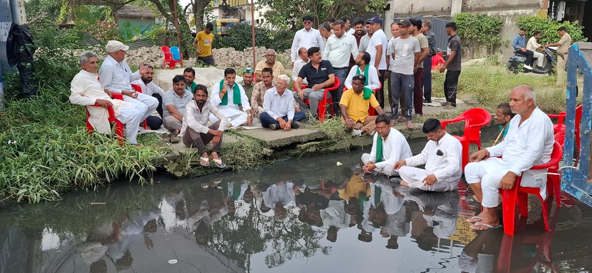 Meerut News: सर्विस रोड पर जलभराव के बीच भाकियू कार्यकर्ताओं ने बैठकर दिया धरना