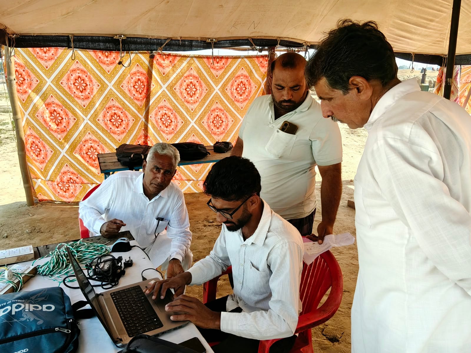 मंडी में बिजली गुल होने पर बाहर से लैपटॉप चार्ज करने के बाद बायोमेट्रिक करता कर्मचारी। 