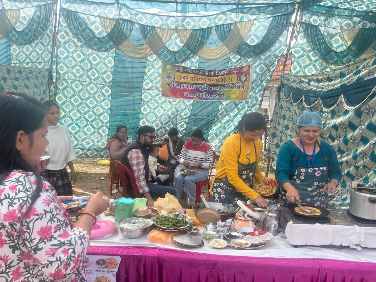 रेड क्रॉस मेले में मक्की की रोटी बनाती महिला ओर उसका आंनद लेते लोग : संवाद