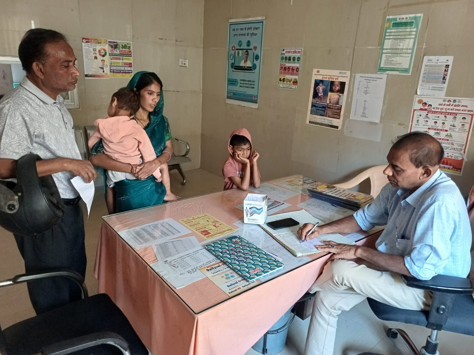 रॉबर्ट्सगंज नगरीय प्राथमिक स्वास्थ्य केंद्र में छोटे बच्चों को उपचार कराने पहुंचे दंपती से पूछत