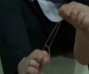 man threads eye of a needle with his toes