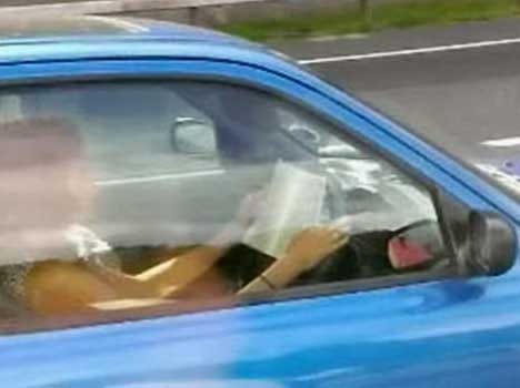 women drives car while reading a book