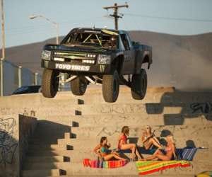 daredevil racing driver drives jumps over bikini clad girls